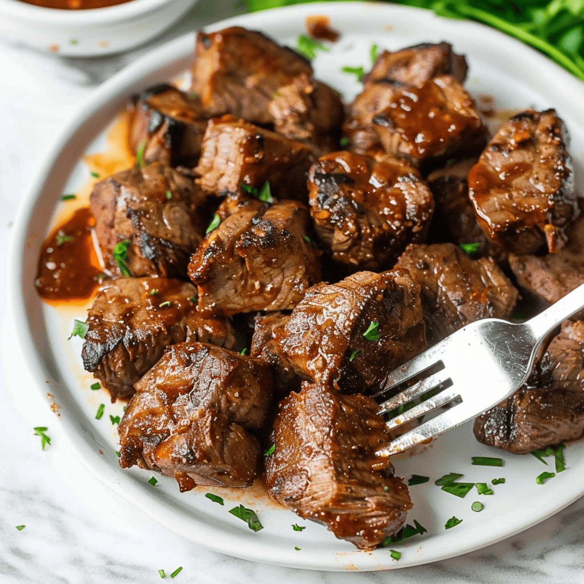 Steak cut into bite size drizzled with BBQ sauce served on a white plate.