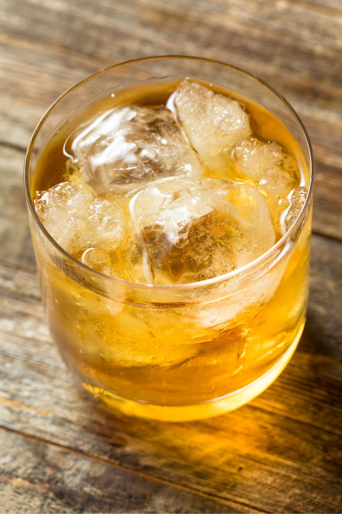 Old fashion glass filled with ice and Godfather cocktail placed on top of a wooden table. 