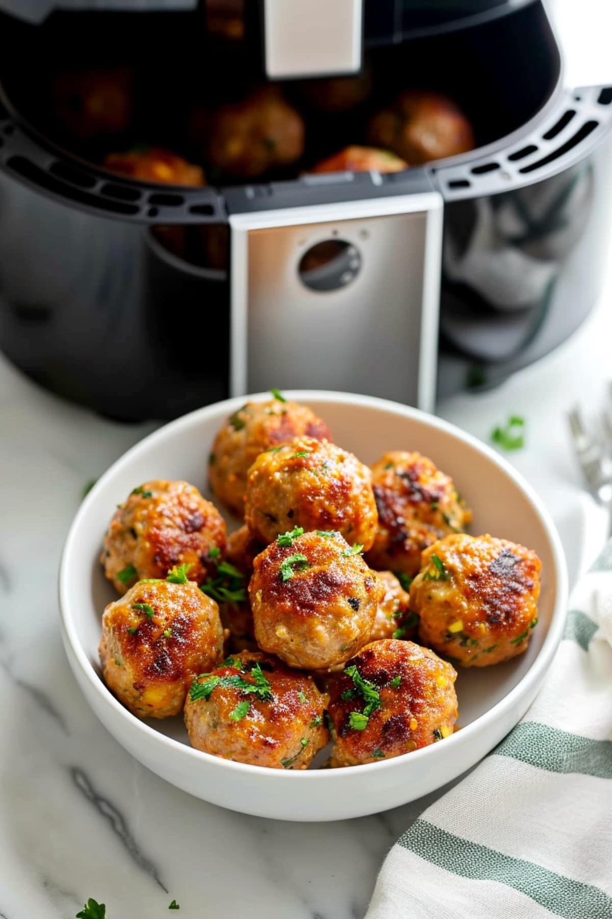 Bowl of turkey meatballs showing an air fryer in the background on a white marble table