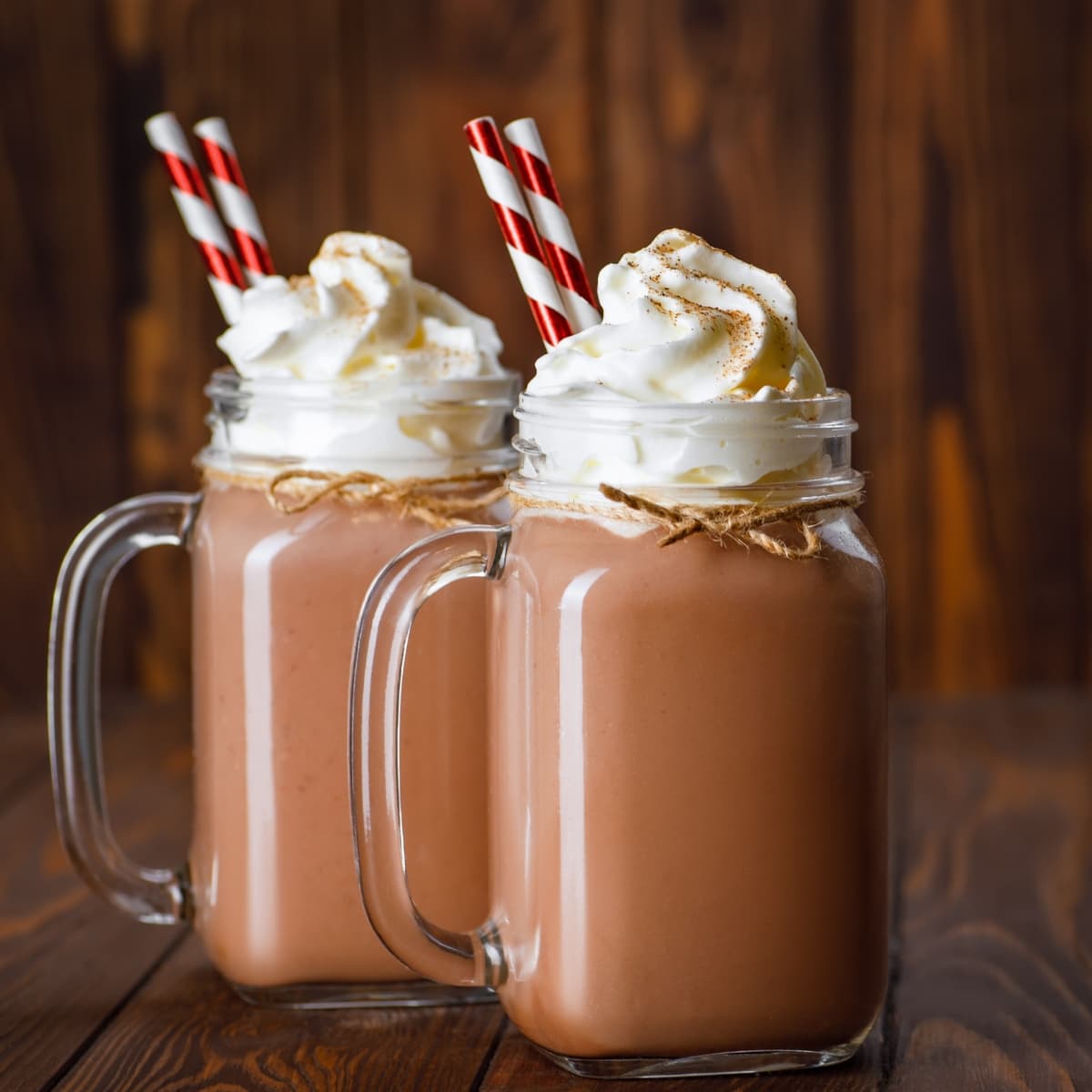 Two glasses of chocolate milkshake with straw topped with whipped cream.