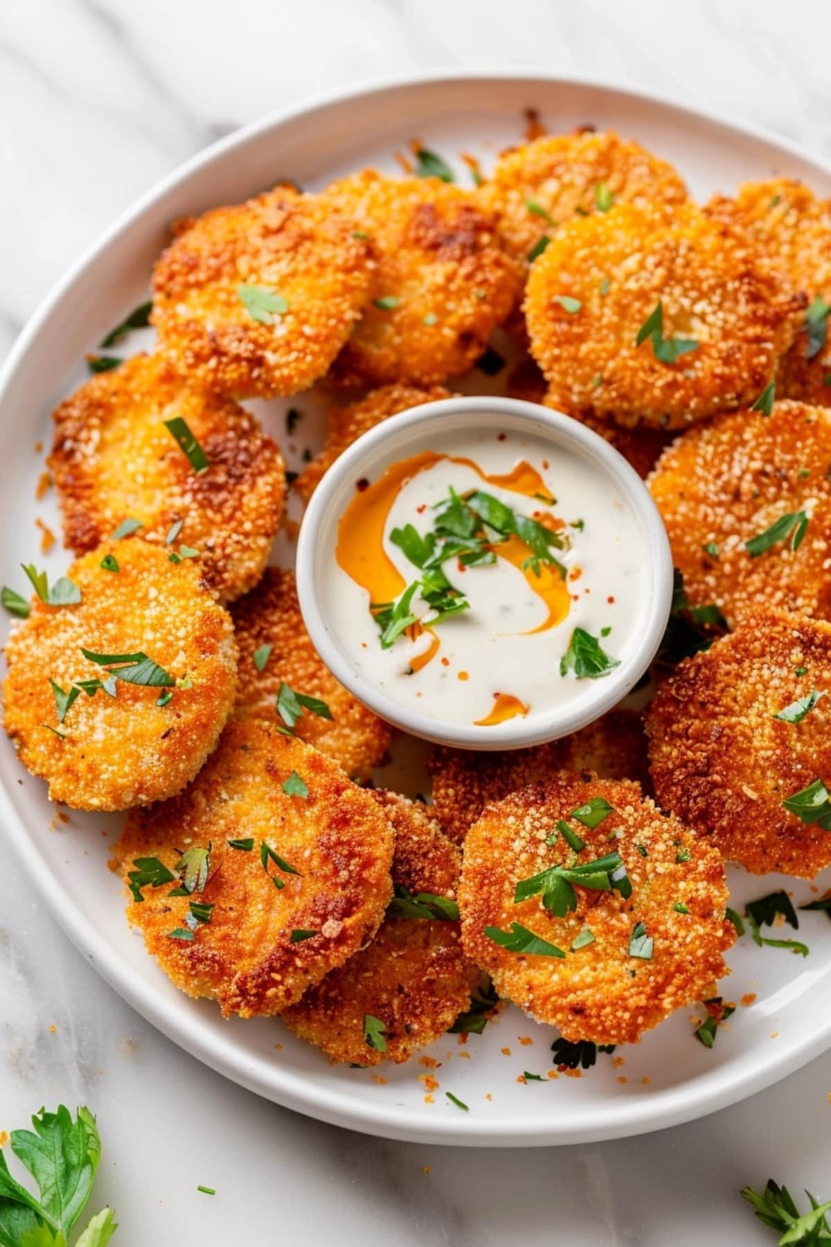 Air fried coated dill pickles with dip on a white plate.