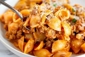 Spoonful shells in creamy and beefy tomato sauce from a white plate.