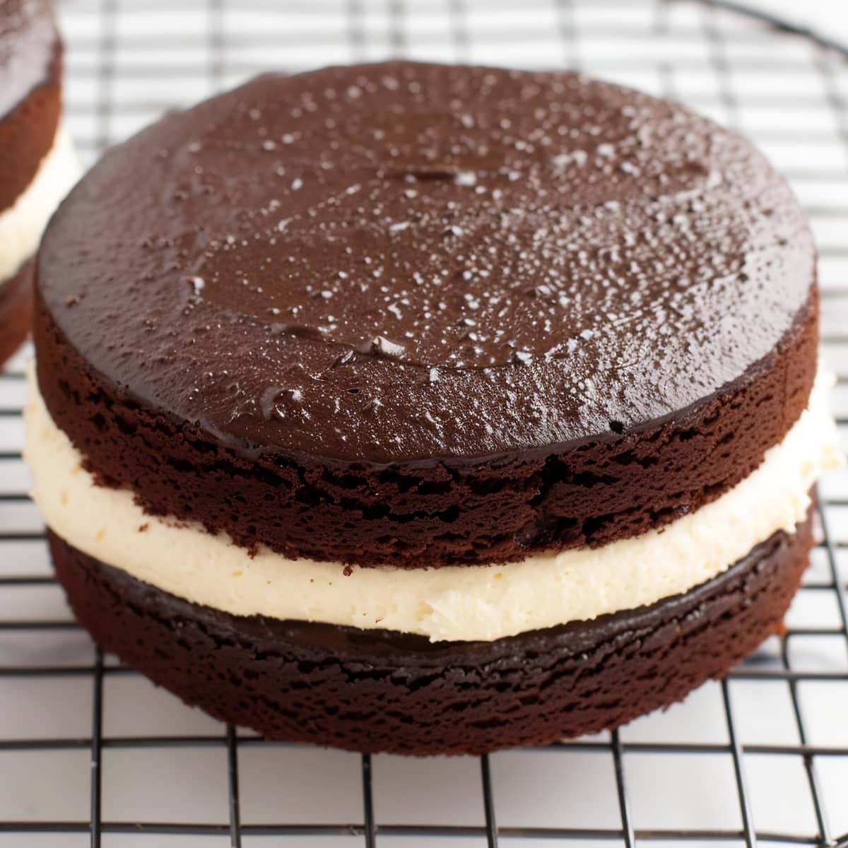 Chocolate cake with buttercream filling and chocolate ganache at the top on a cooling rack