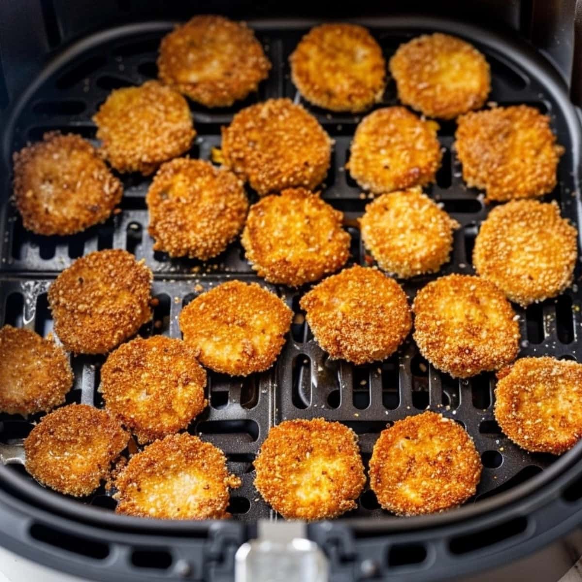 Coated dill pickles inside an air fryer basket.