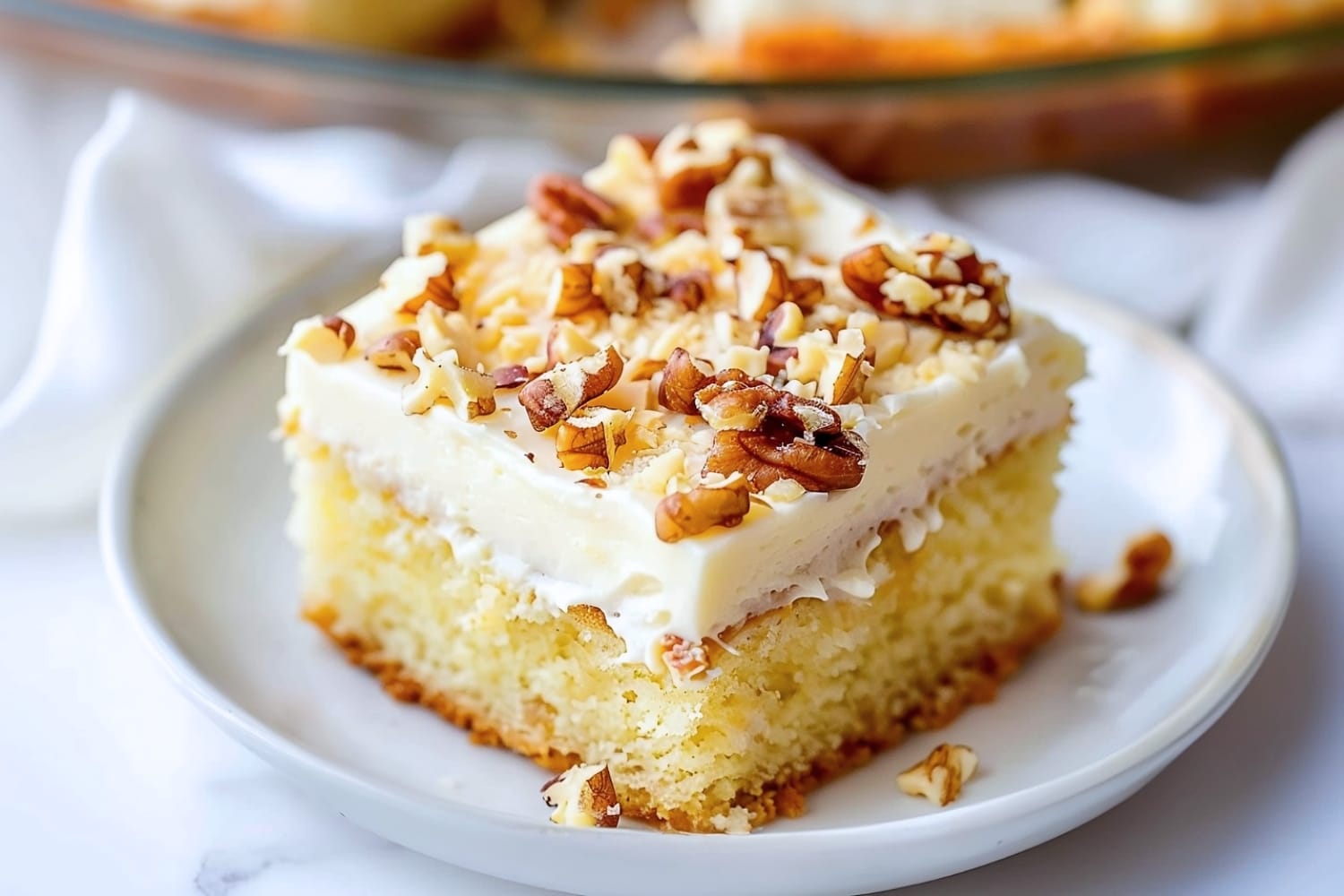 A slice of cake with chopped pecans and cream cheese frosting sitting in a white plate