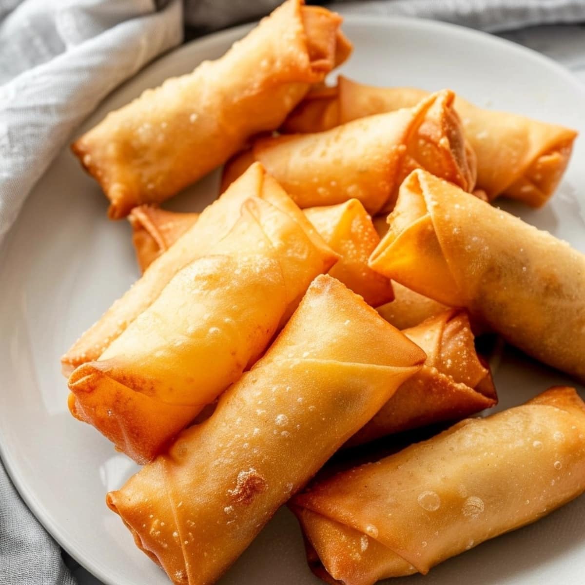 Bunch of crunchy egg rolls in a white plate.