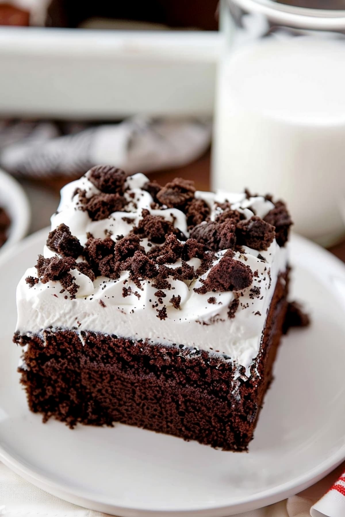 A slice of homemade oreo poke cake next to a glass of milk