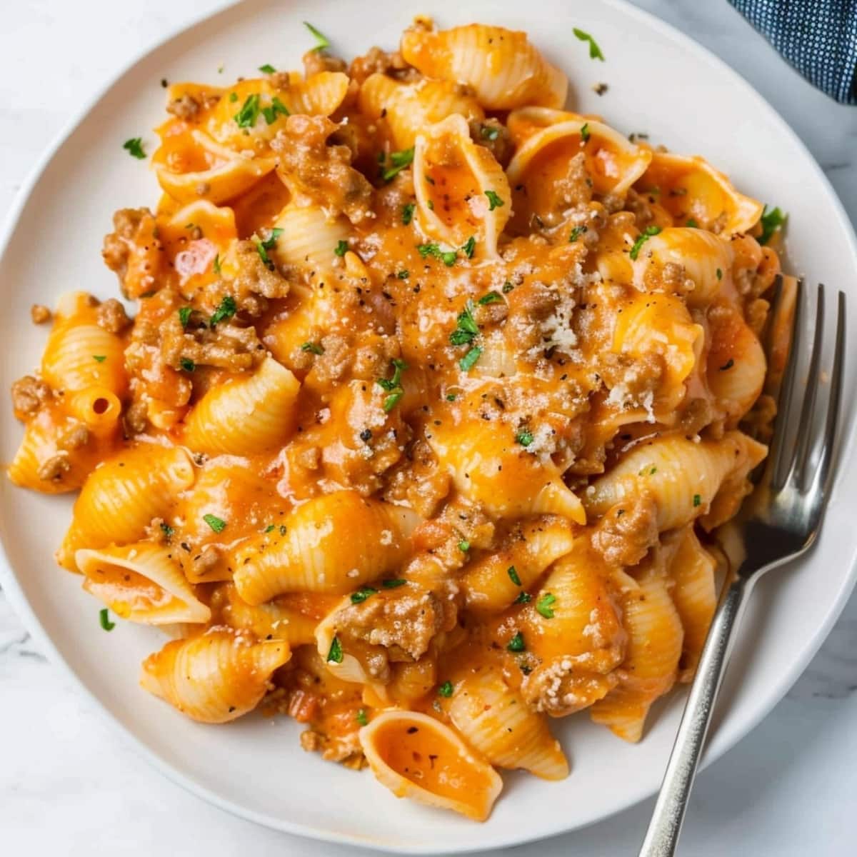 Top view of a serving of beef and shell pasta with cheesy sauce on a white plate.