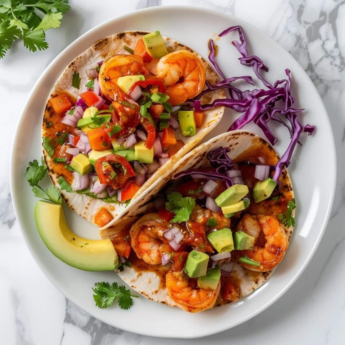 Tacos with shrimp, diced avocado, shredded red cabbage, onion, and salsa on top of white marble.