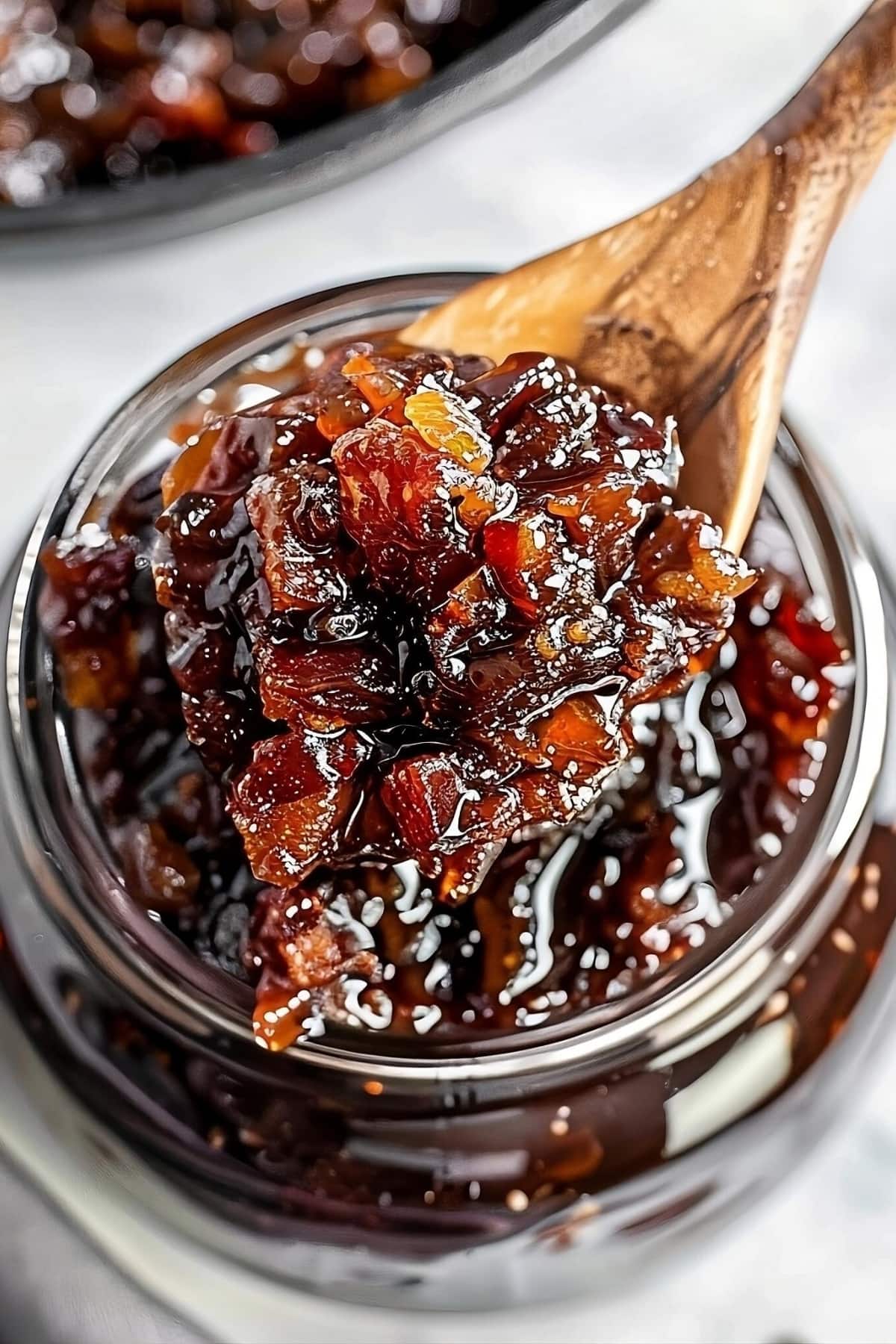 Wooden spoon scooping bourbon bacon jam from a glass jar
