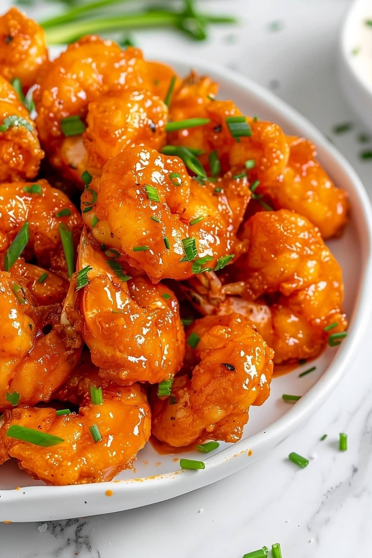 Shrimp with buffalo sauce in a white plate garnished with chopped leeks.