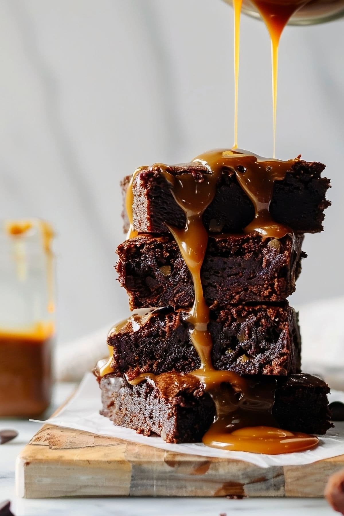 Stack of Caramel Brownies Drizzled with Caramel and a Jar of Caramel in the Background