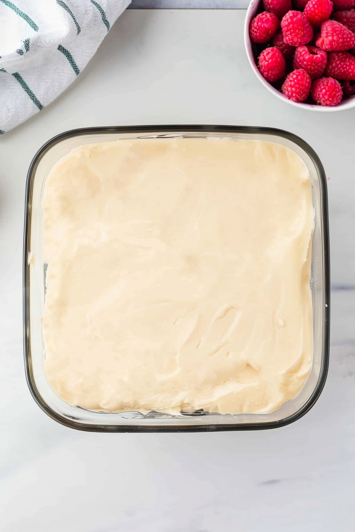 Cheesecake filling in a glass baking dish with fresh raspberries, overhead view