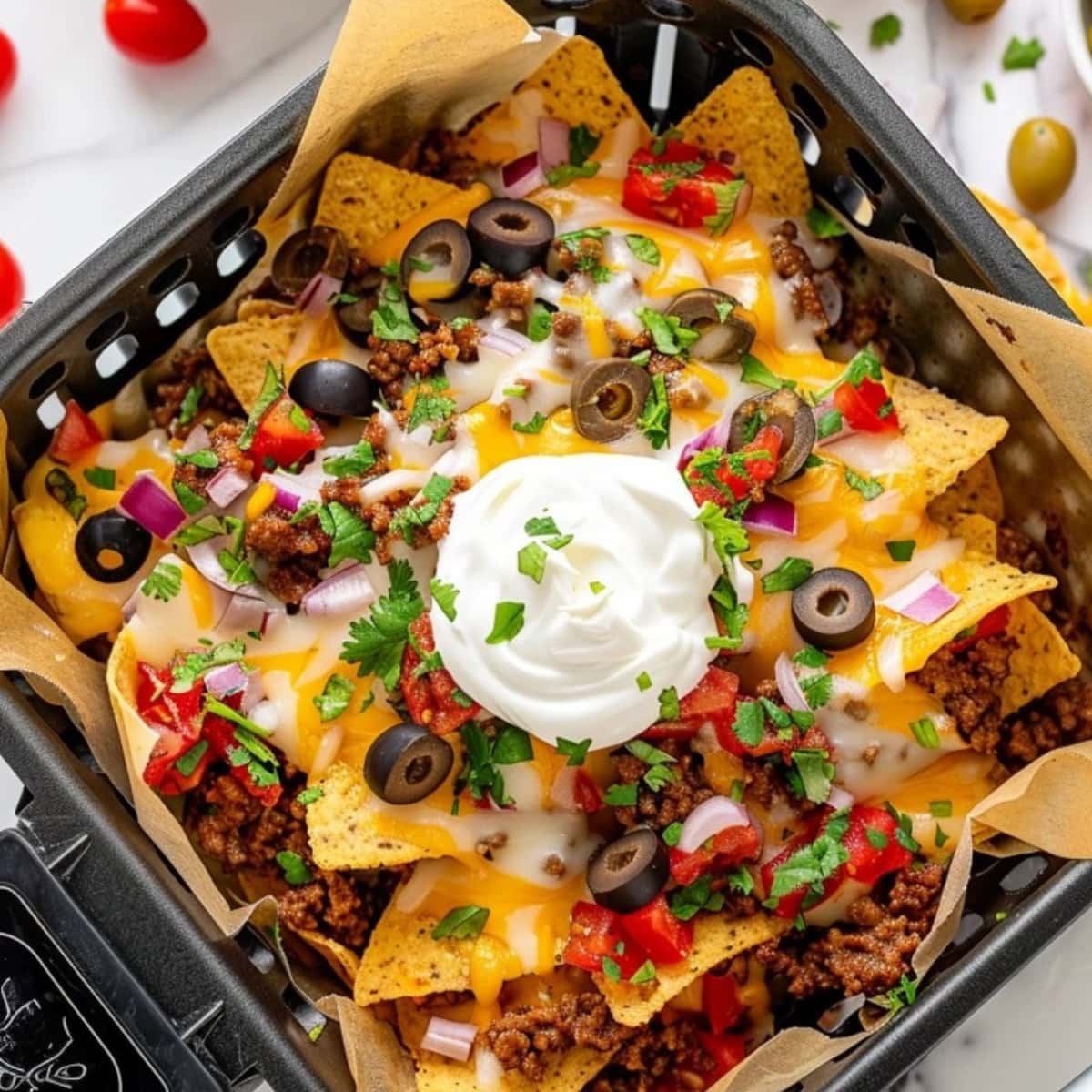 Air Fryer Nachos in an air fryer basket with sour cream on top.