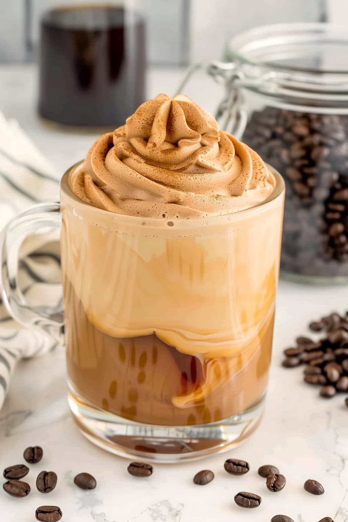 A glass mug latte with whipped cream on a marble countertop