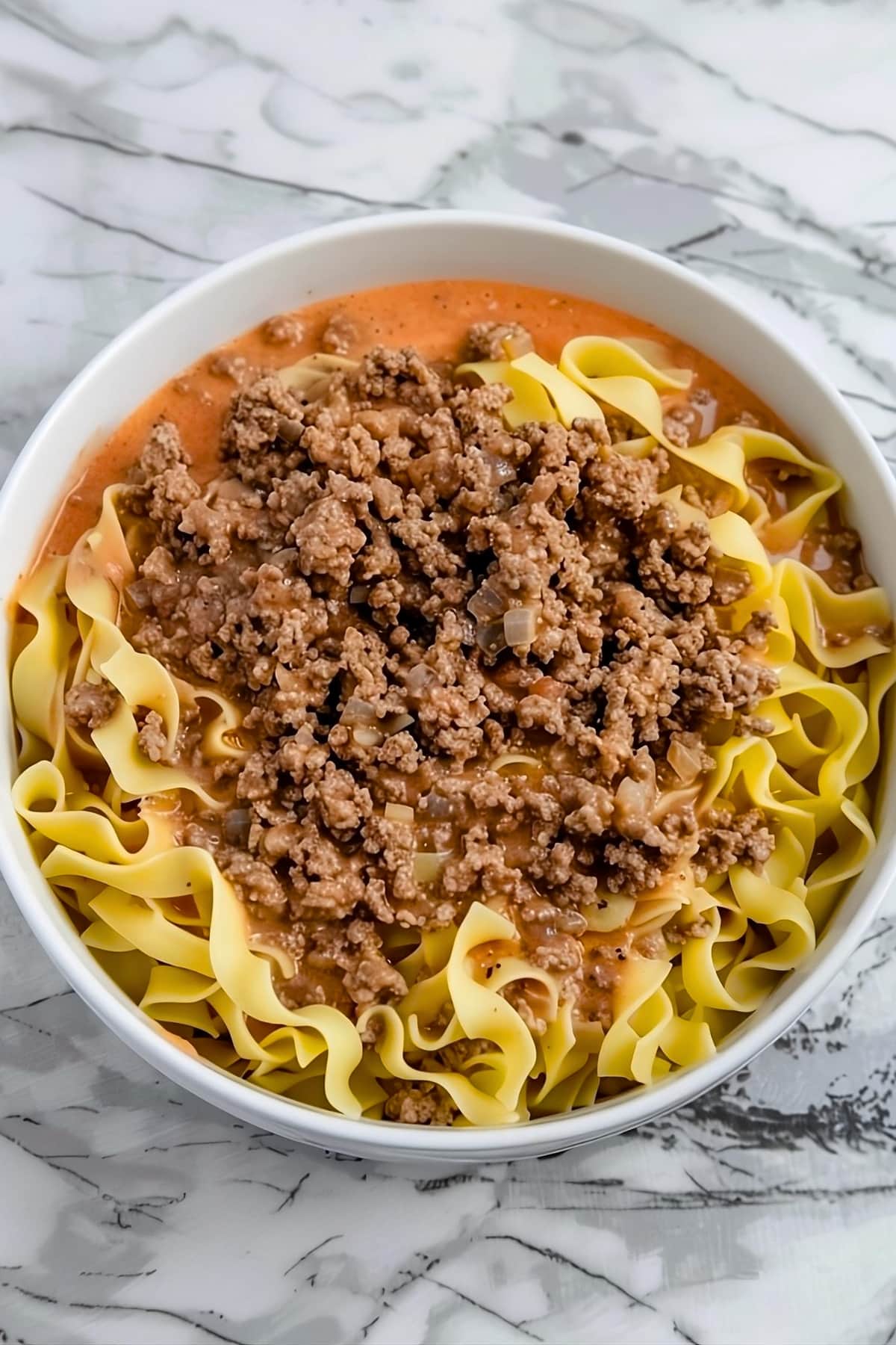 Cooked beef and noodles tossed in soup mixture in a white bowl.