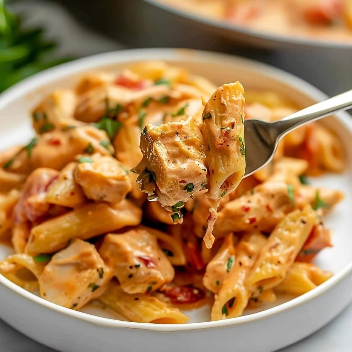 Fork with penne pasta and chicken from Tuscan chicken pasta in a plate.