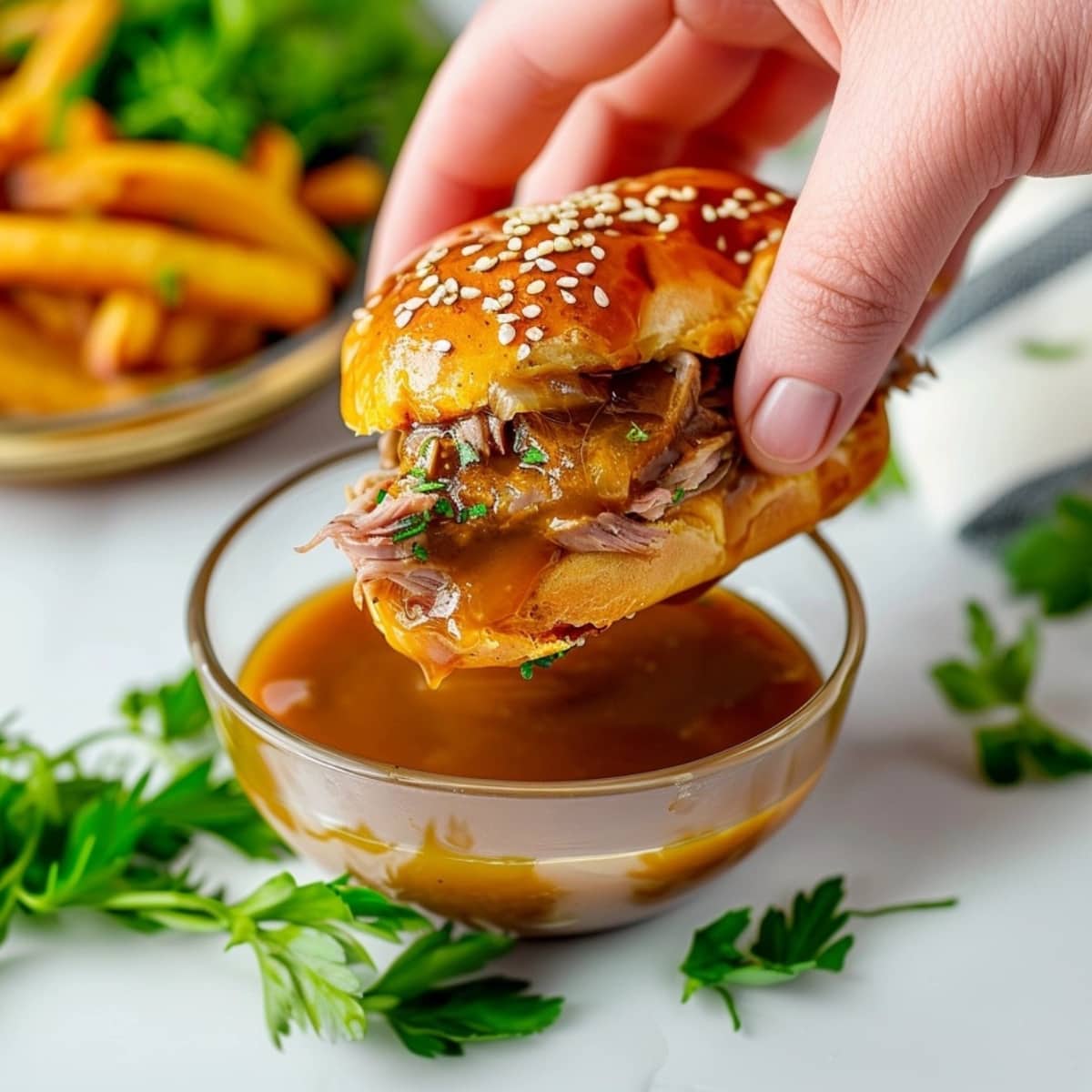 French dip sliders dipped in au jus gravy in a glass bowl.