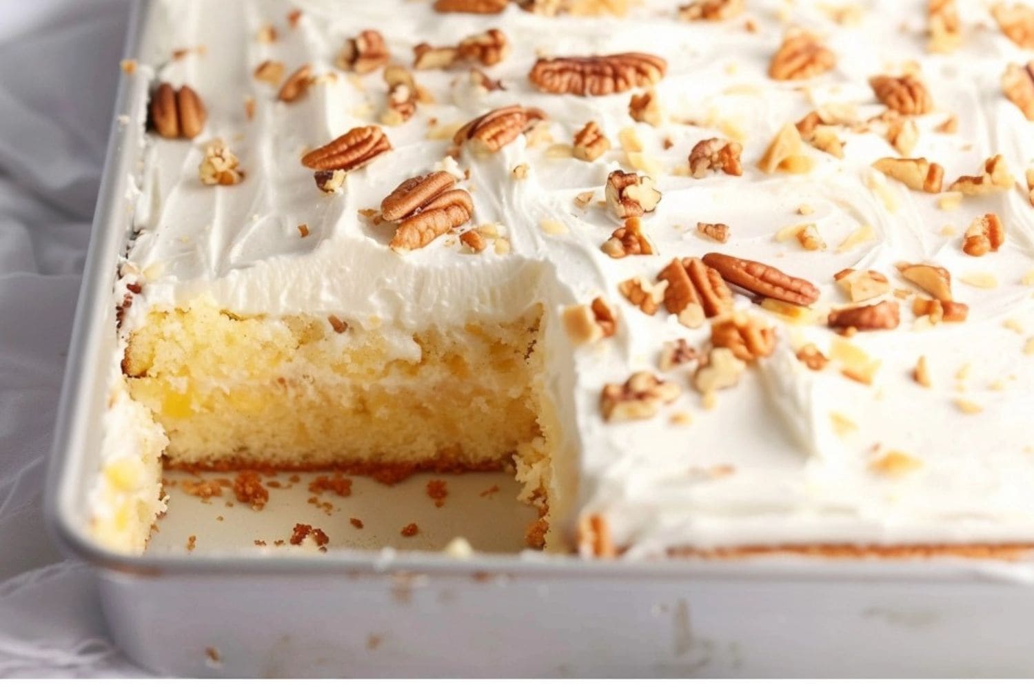 Pineapple sheet cake in a baking pan, portion slice missing.