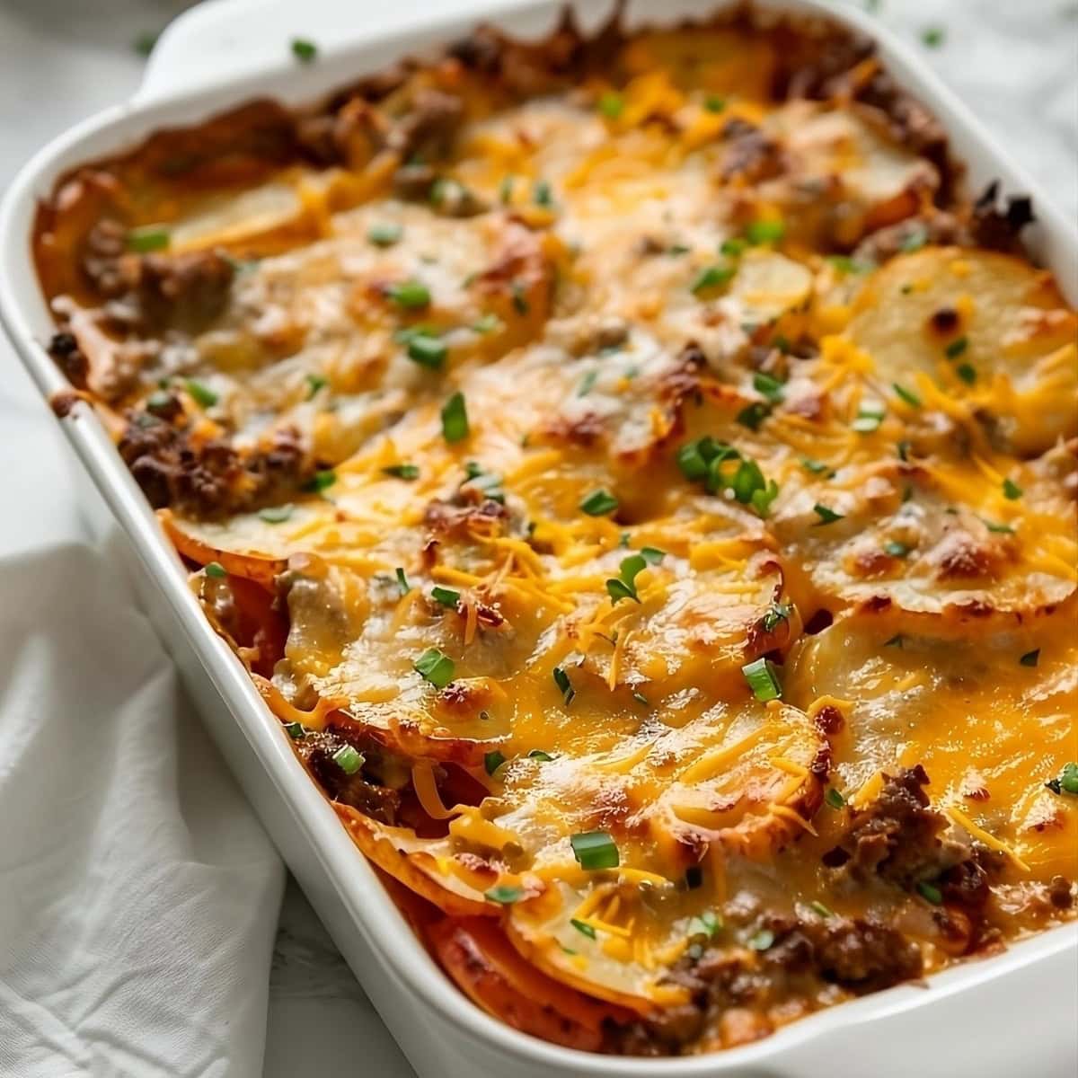 Cheesy sausage potato casserole in a white rectangular baking dish.