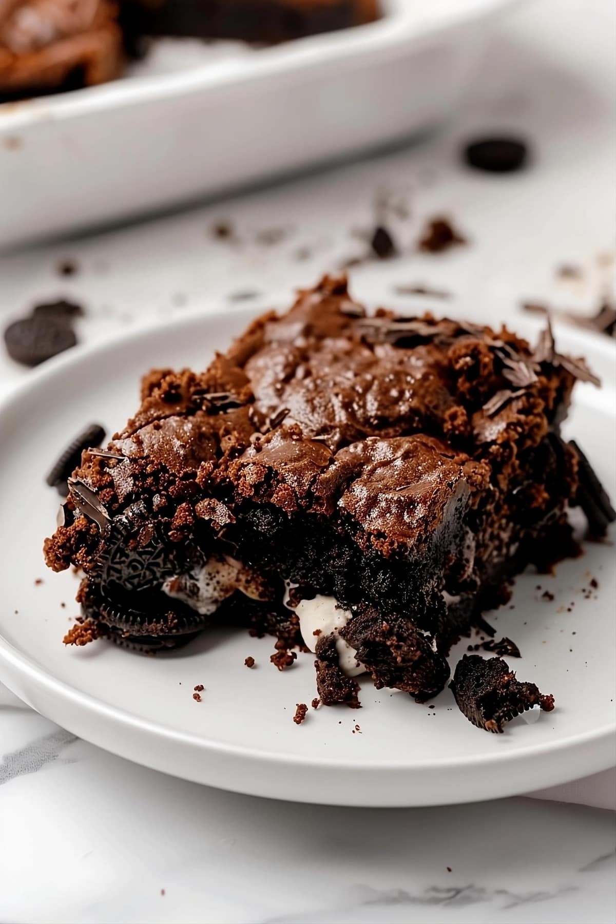 Slice of Oreo dump cake in a white plate on a white marble table.