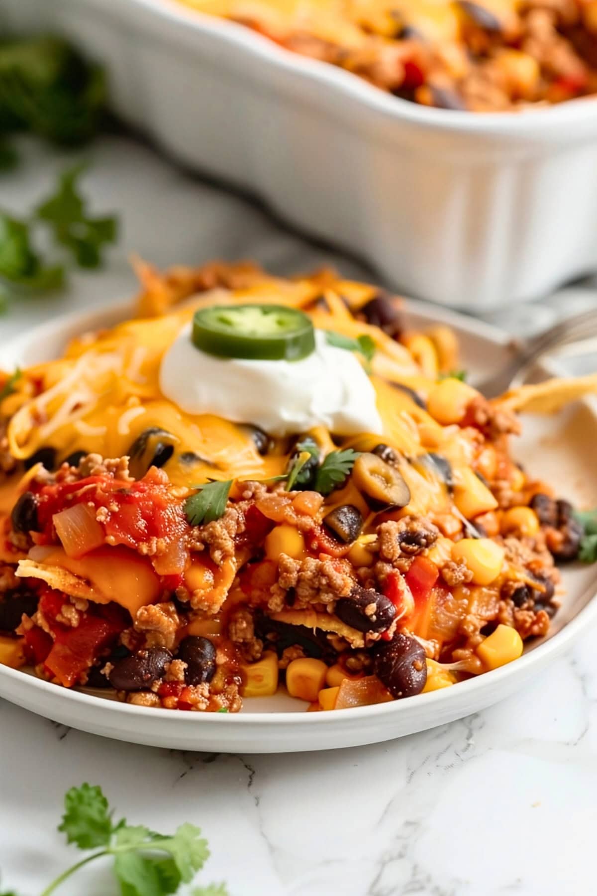 A serving of taco casserole in a white plate garnished with sour cream.