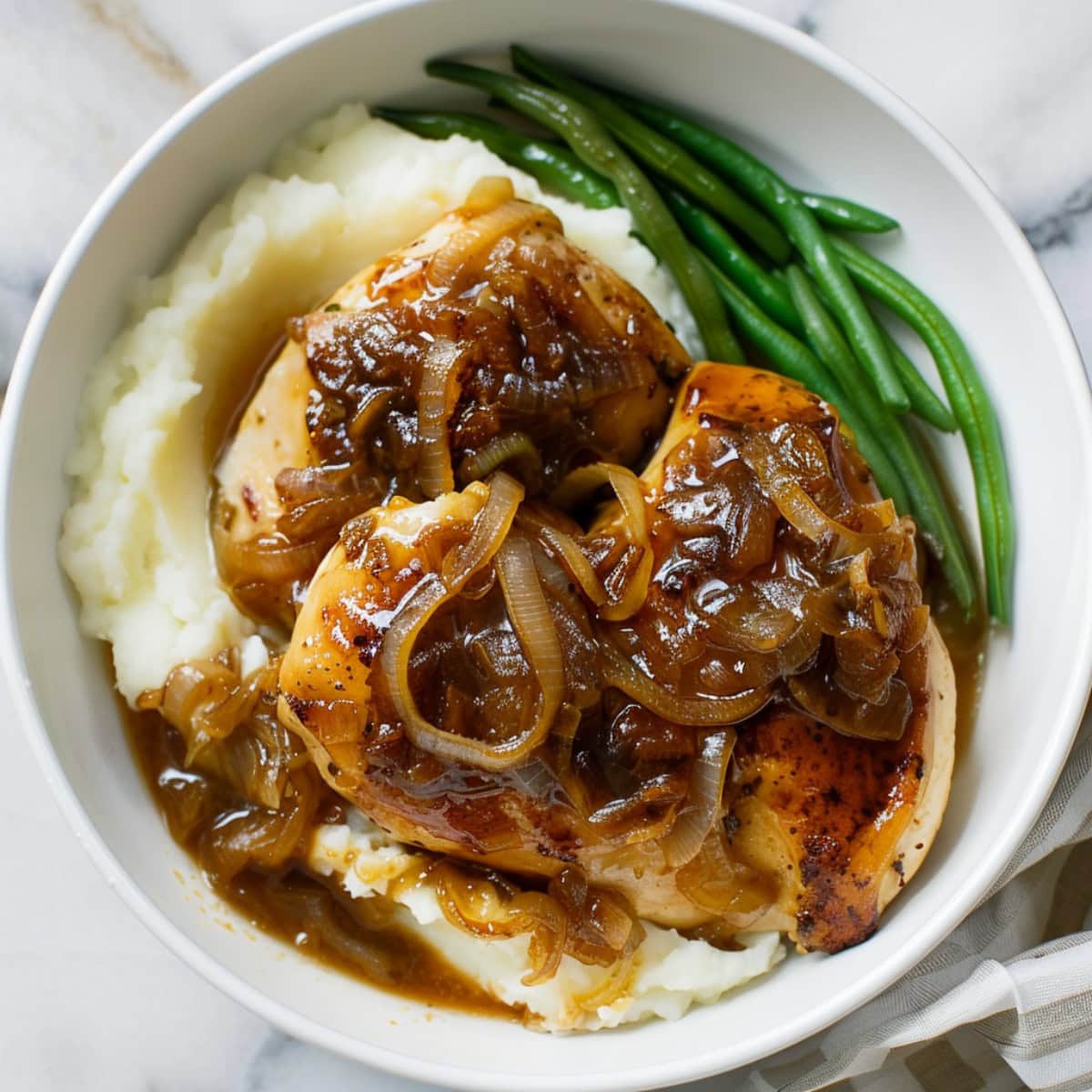 French onion chicken plated alongside a mashed potato and green beans