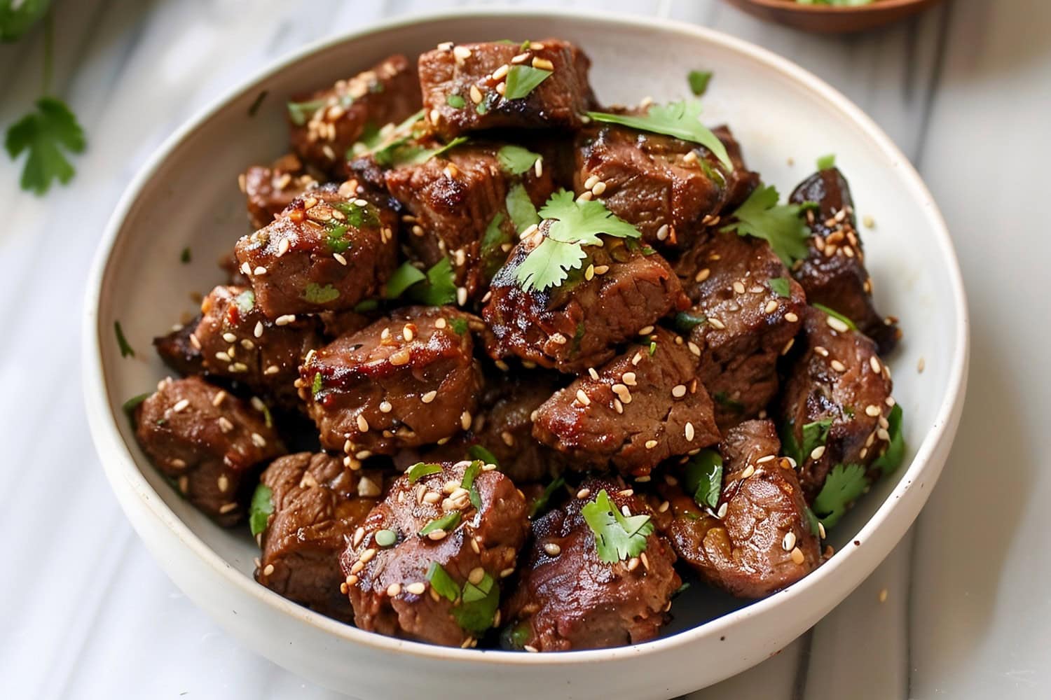 A bowl of Asian steak bites served with white rice on a white marble countertop