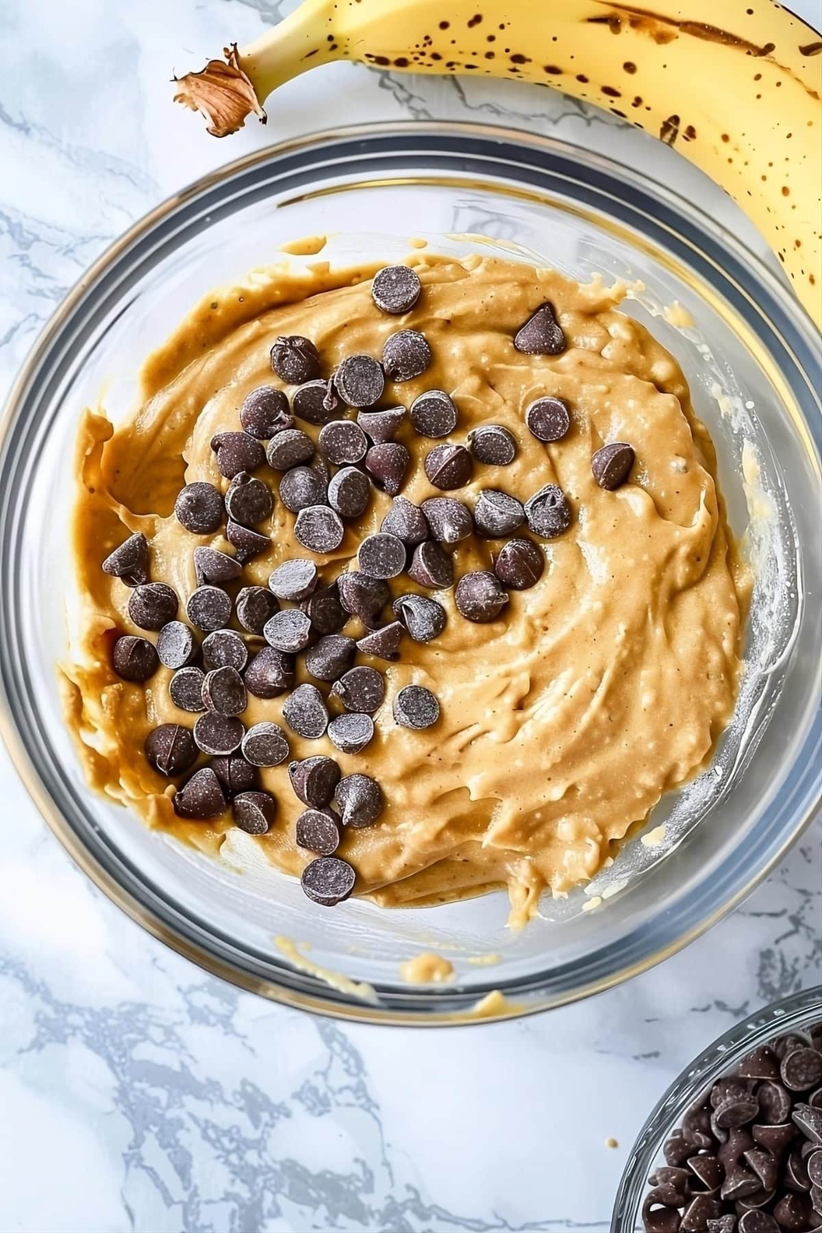 Banana bread batter with chocolate chips mixed in a glass bowl, top down view.