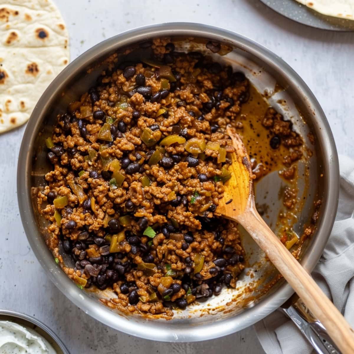 Ground beef, black beans and green chilis mixed in a stainless pan with olive oil.