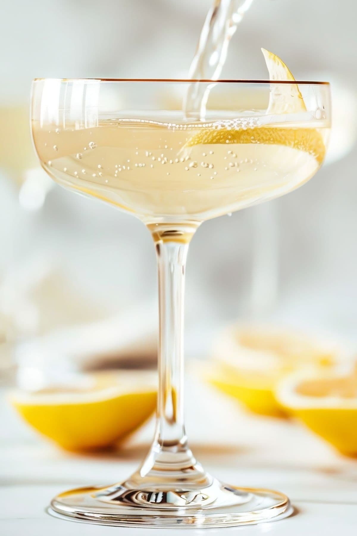 Close Up of Bee's Knees Cocktail Being Poured into a Glass with a Lemon Peel Twist with Fresh Lemons on the Table Around the Glass