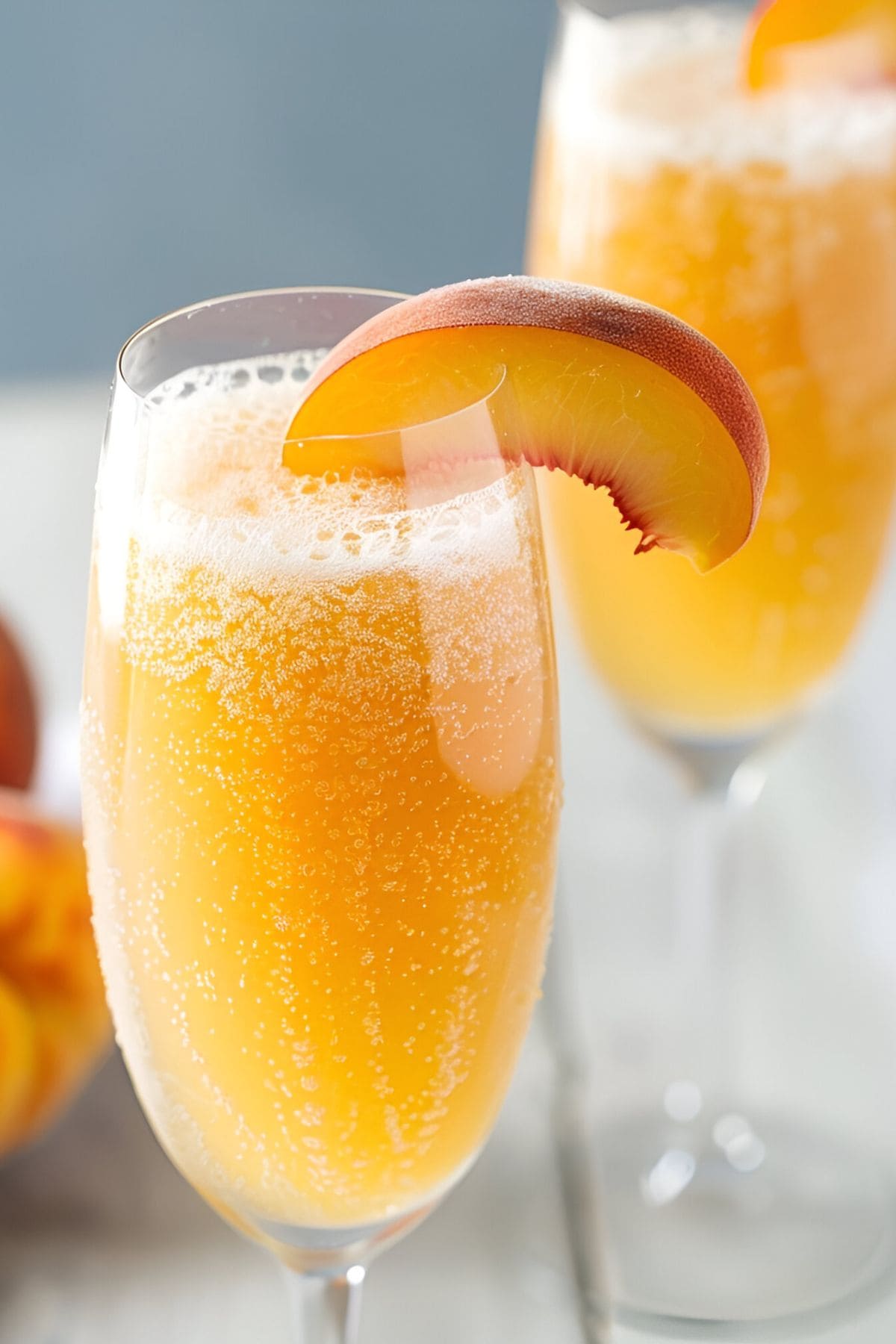 Close Up of Two Peach Bellini in Champagne Flutes with Bubbles and a Fresh Peach Slice