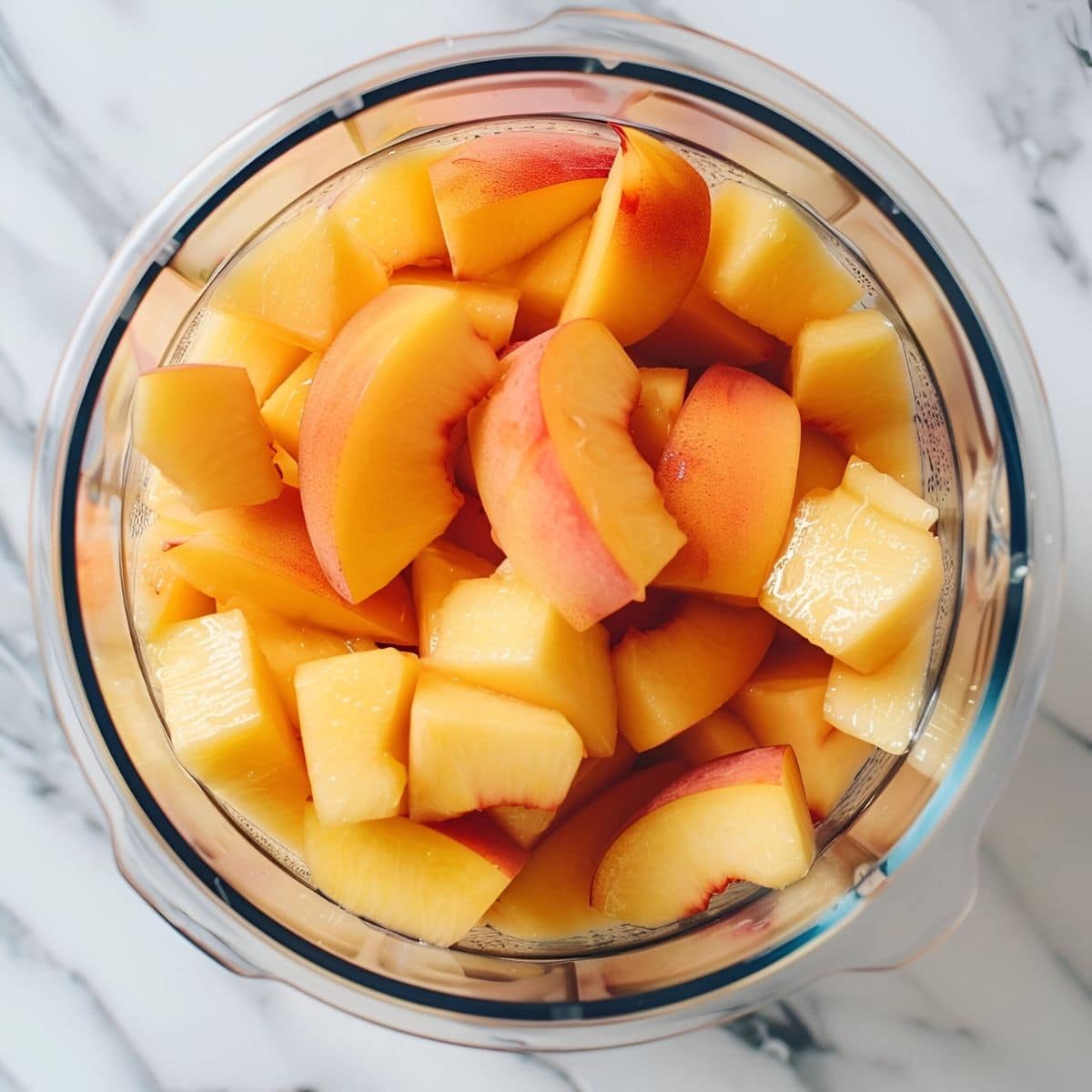 Top View of Fresh Peach Pieces in a Blender on a White Marble Table 
