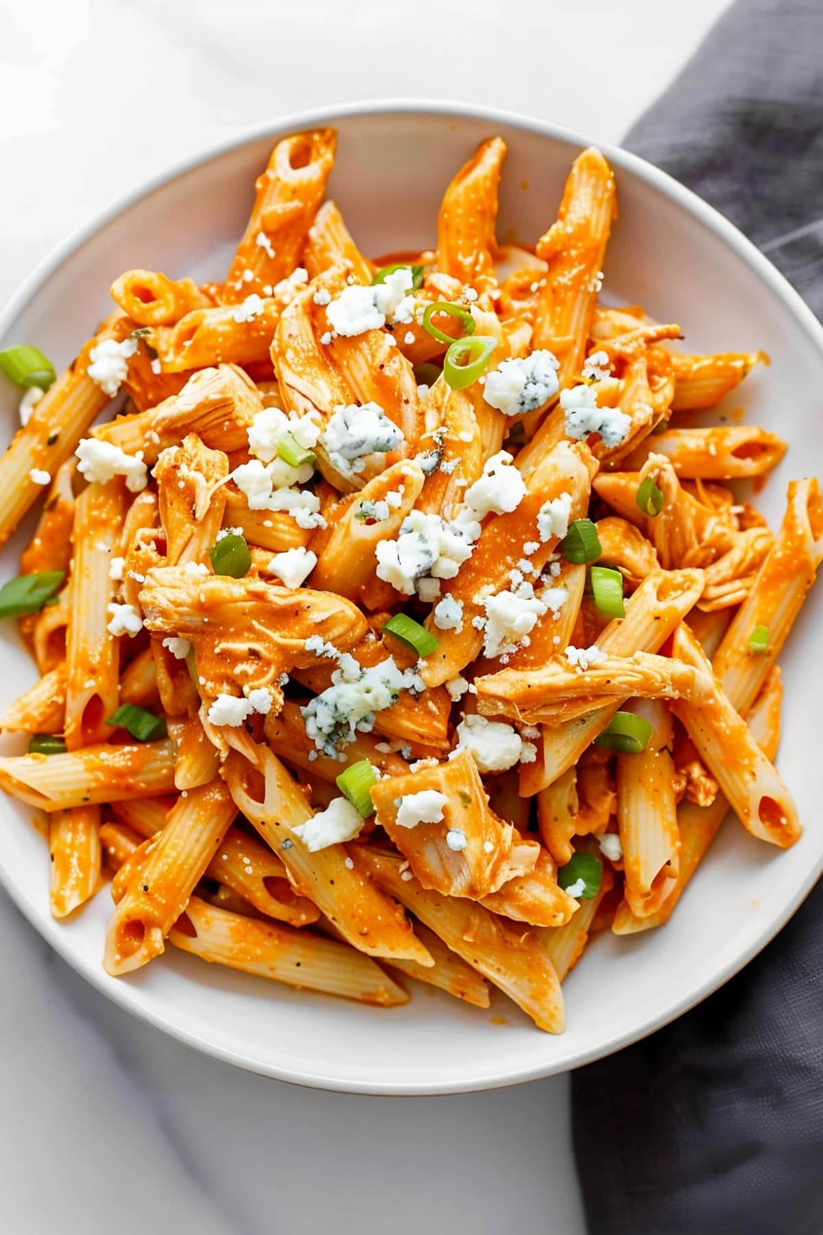 Homemade buffalo chicken pasta, tossed in a creamy sauce and garnished onions and blue cheese