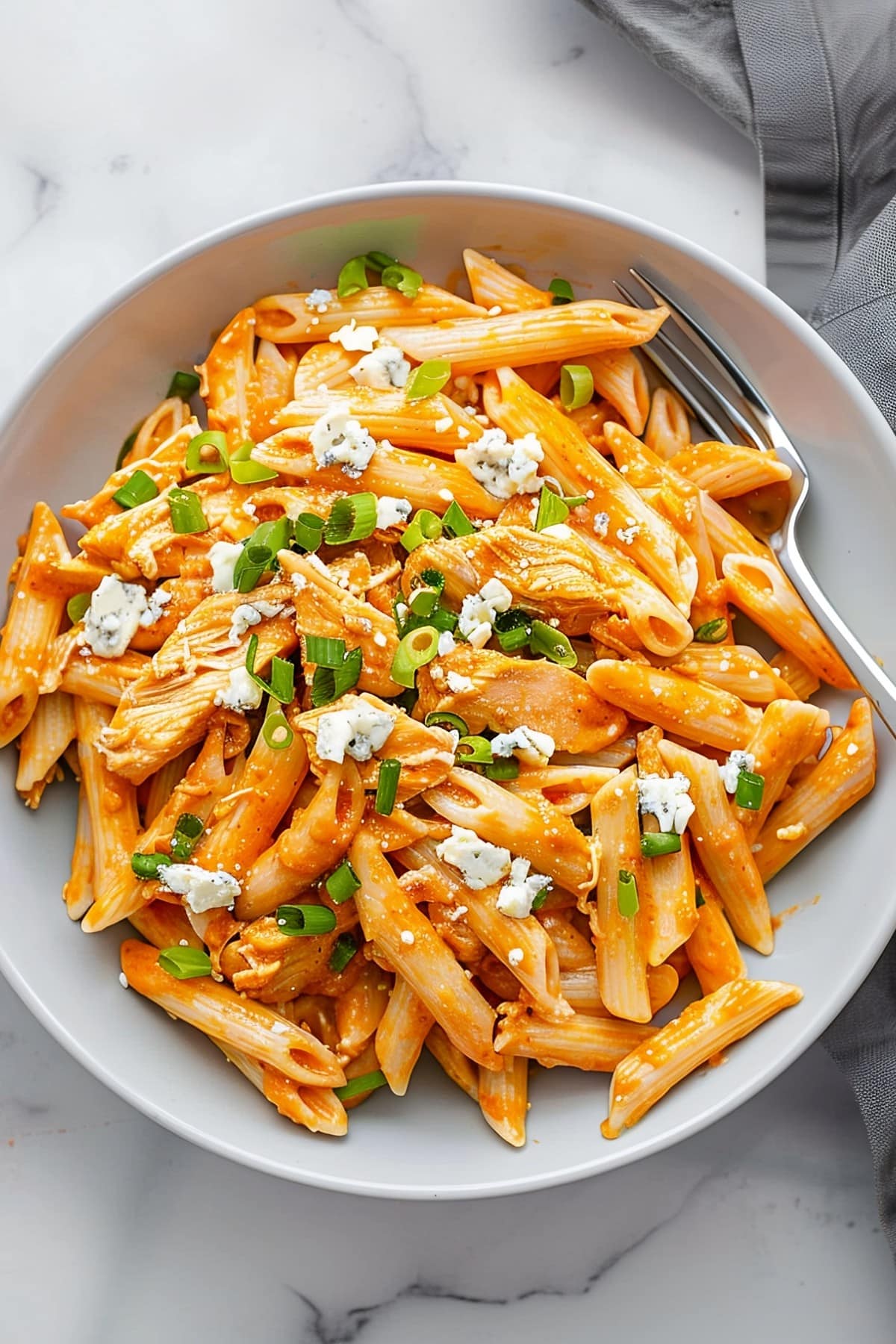 A bowl of buffalo chicken pasta topped with blue cheese and chopped green onions