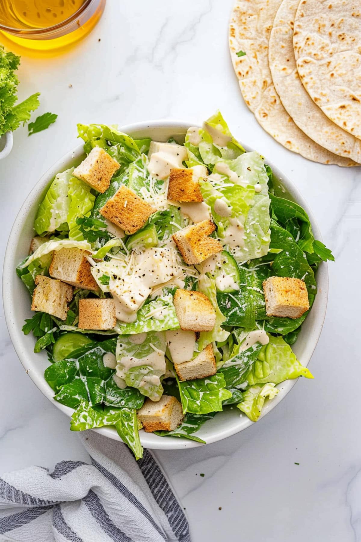 A bowl of Caesar salad with croutons, lettuce and tortilla wraps on the side