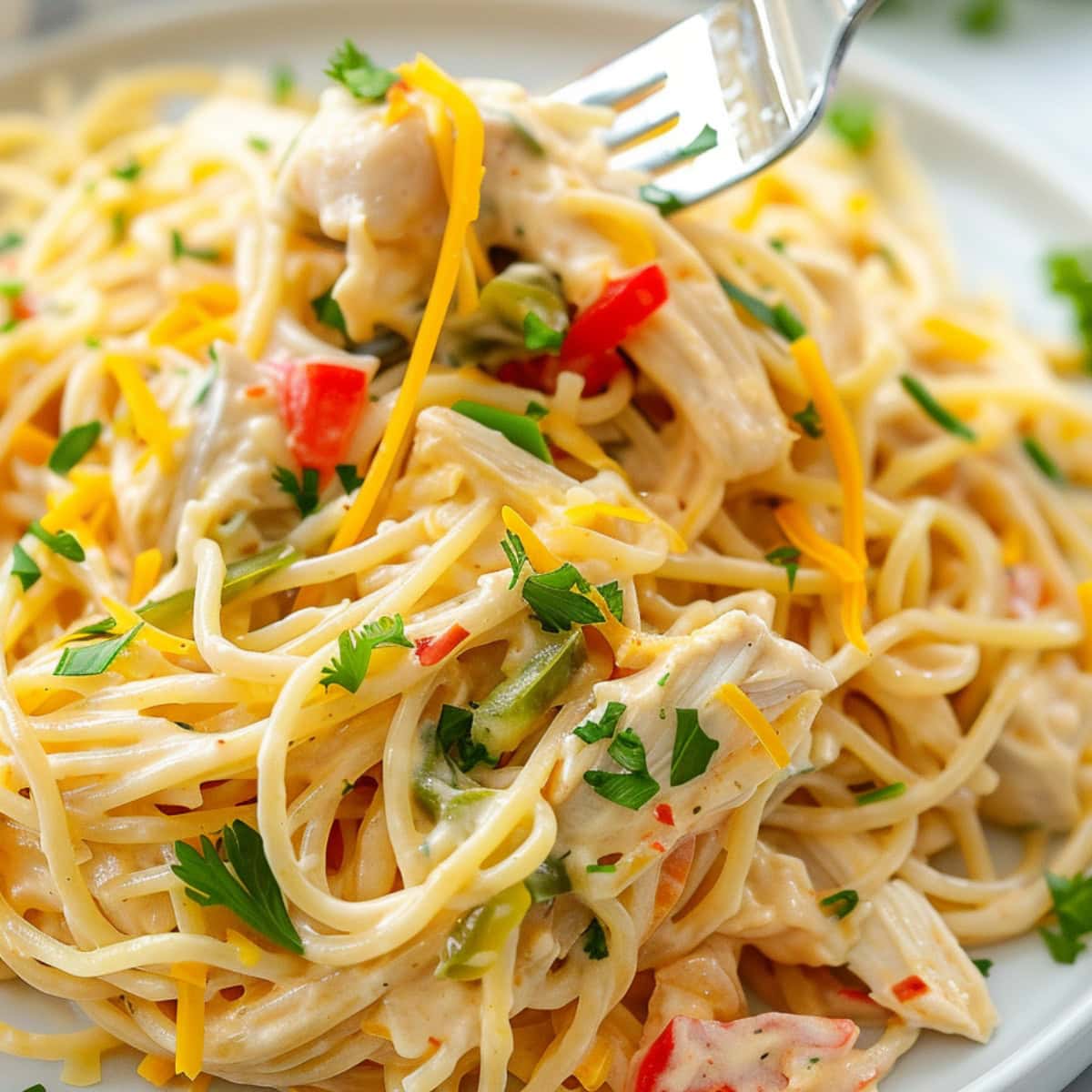 Cheesy chicken spaghetti casserole in plate lifted by fork.