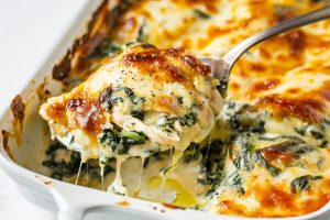 Spoon lifting a serving of chicken with spinach casserole from a white casserole dish.