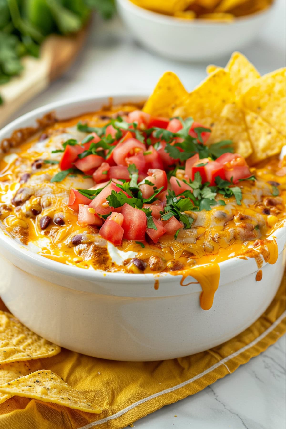 Bowl of cheesy chili dip with tortillos garnished with tomatoes and chopped cilantro leaves.