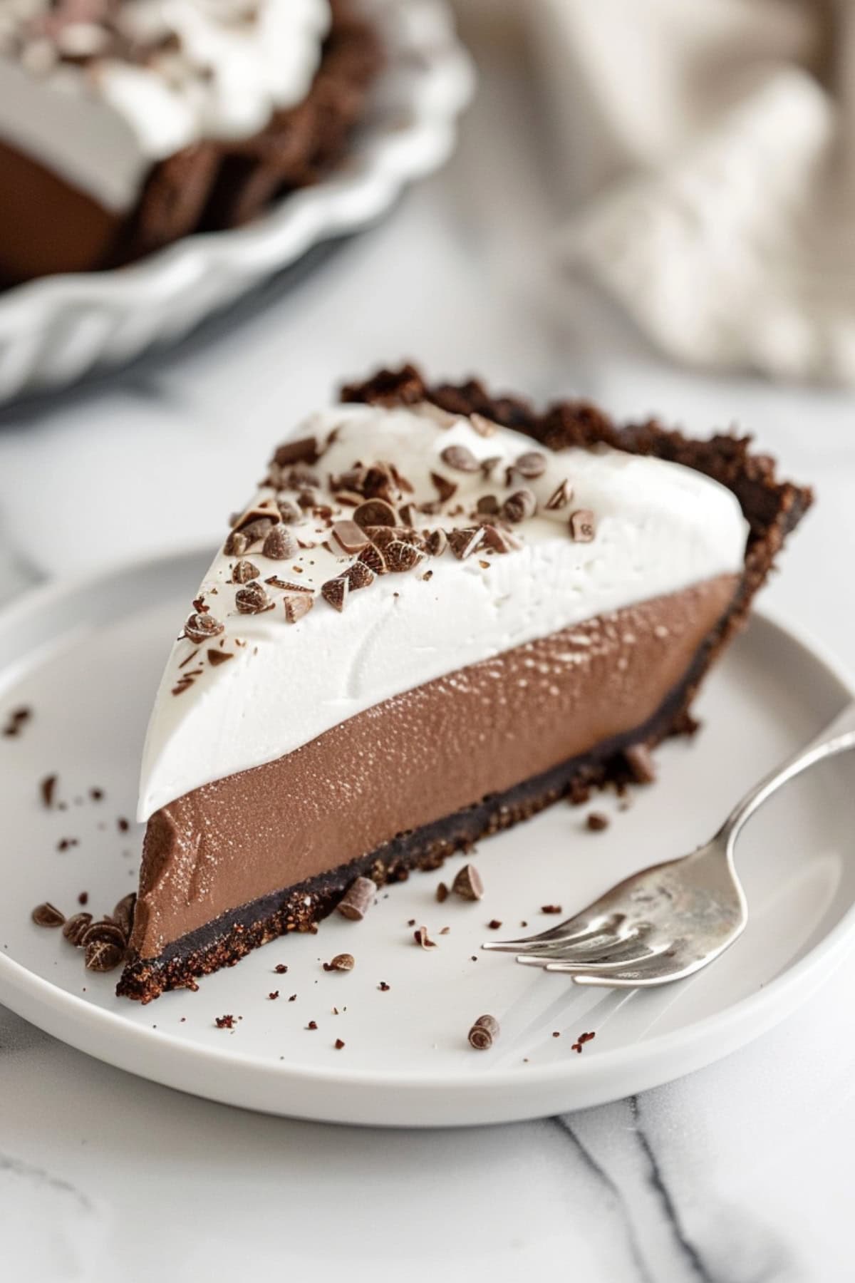 Slice of chocolate cream pie with chocolate chunks on top served on a plate with a fork.