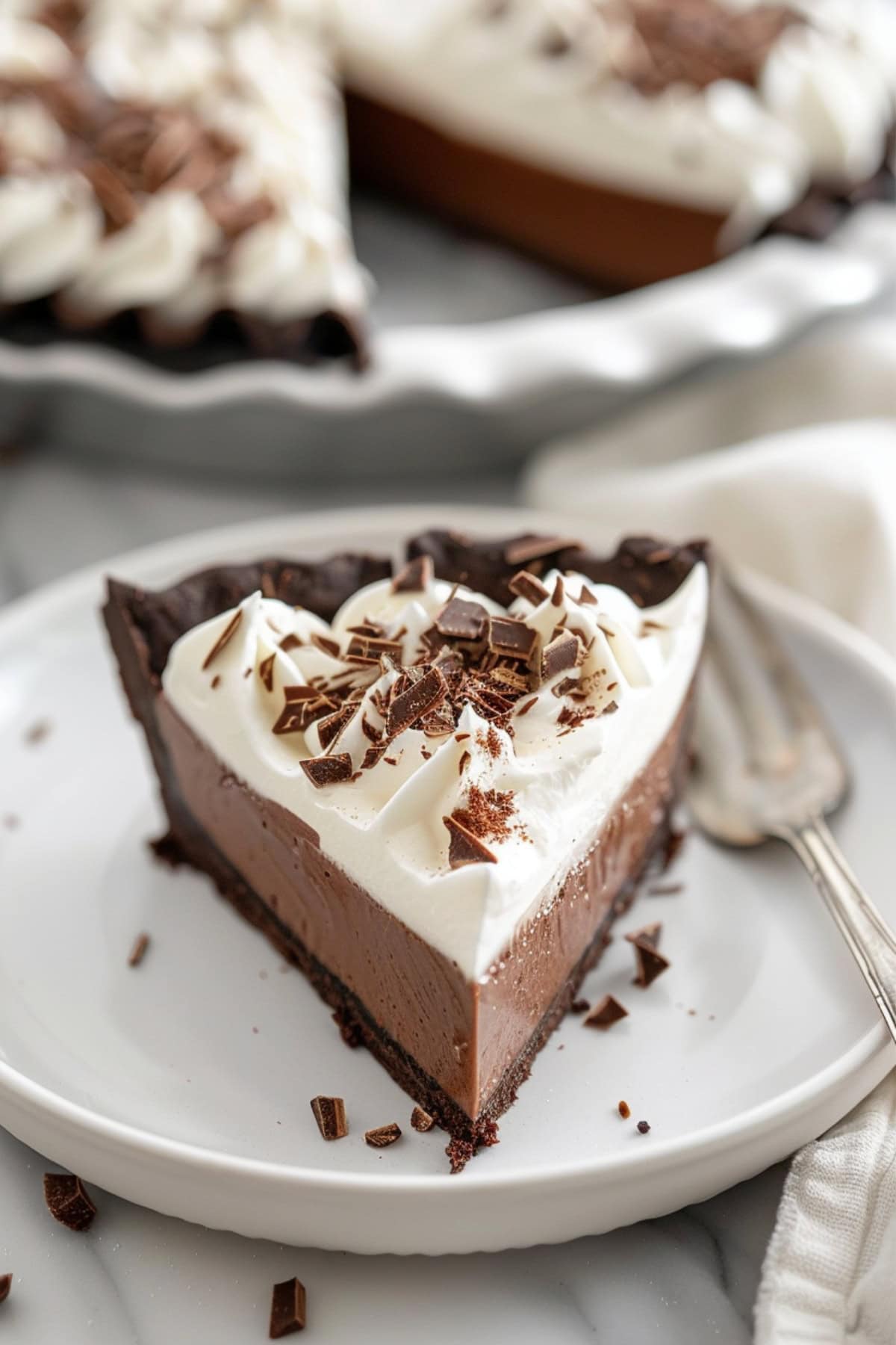 Slice of chocolate cream pie with chocolate shavings served on a white plate.