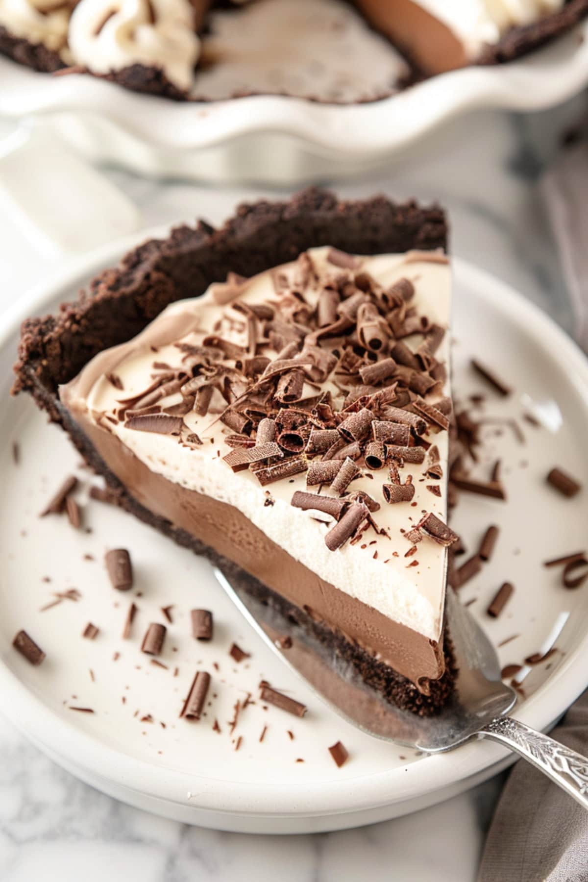 Pie ladle with a slice of creamy chocolate cream pie placed on white plate.