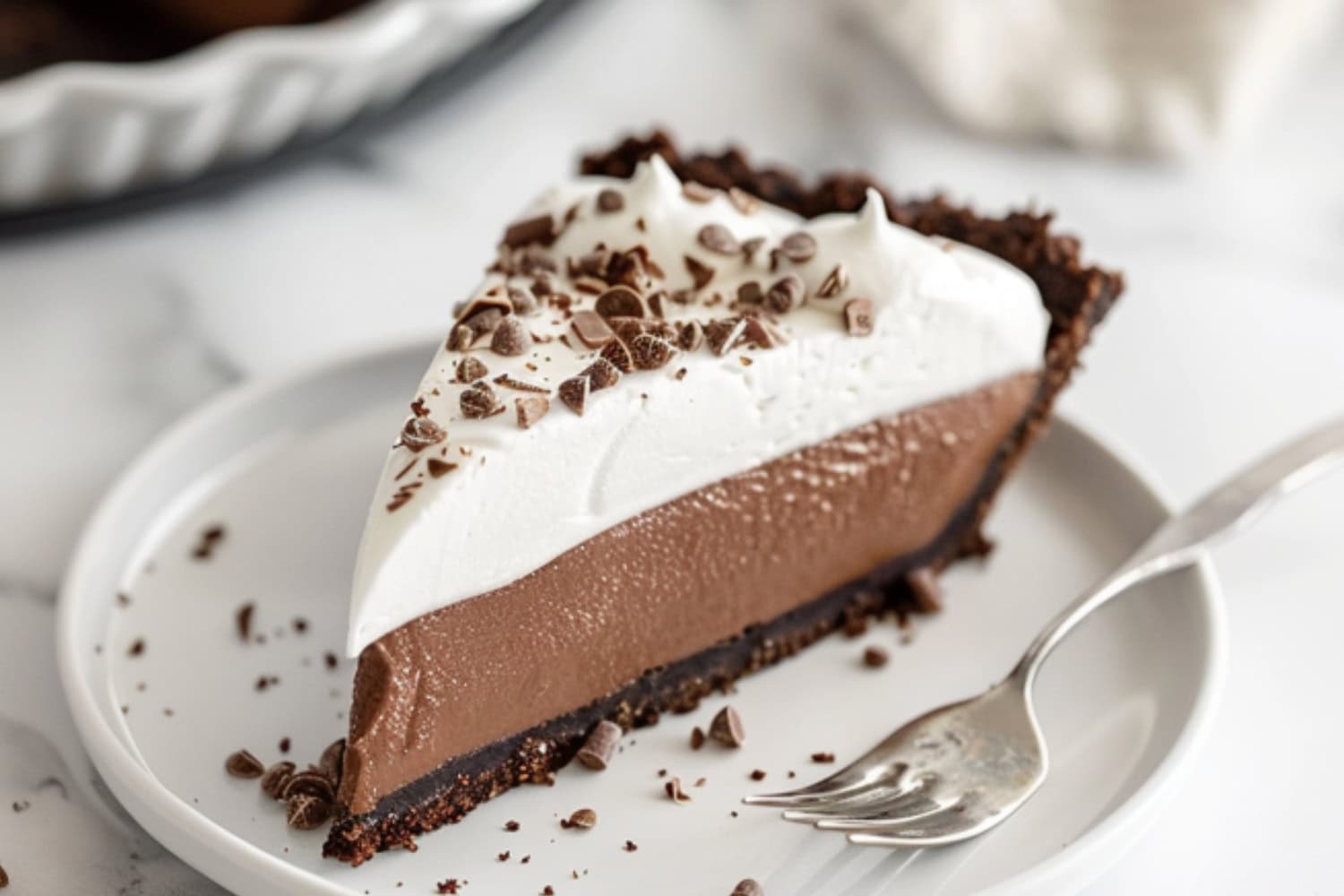 A slice of chocolate cream pie in a white pate with fork.