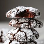 Close Up Stack of Chewy Chocolate Crinkle Cookies Dusted with Powdered Sugar, the Top Cookie Missing a Bite