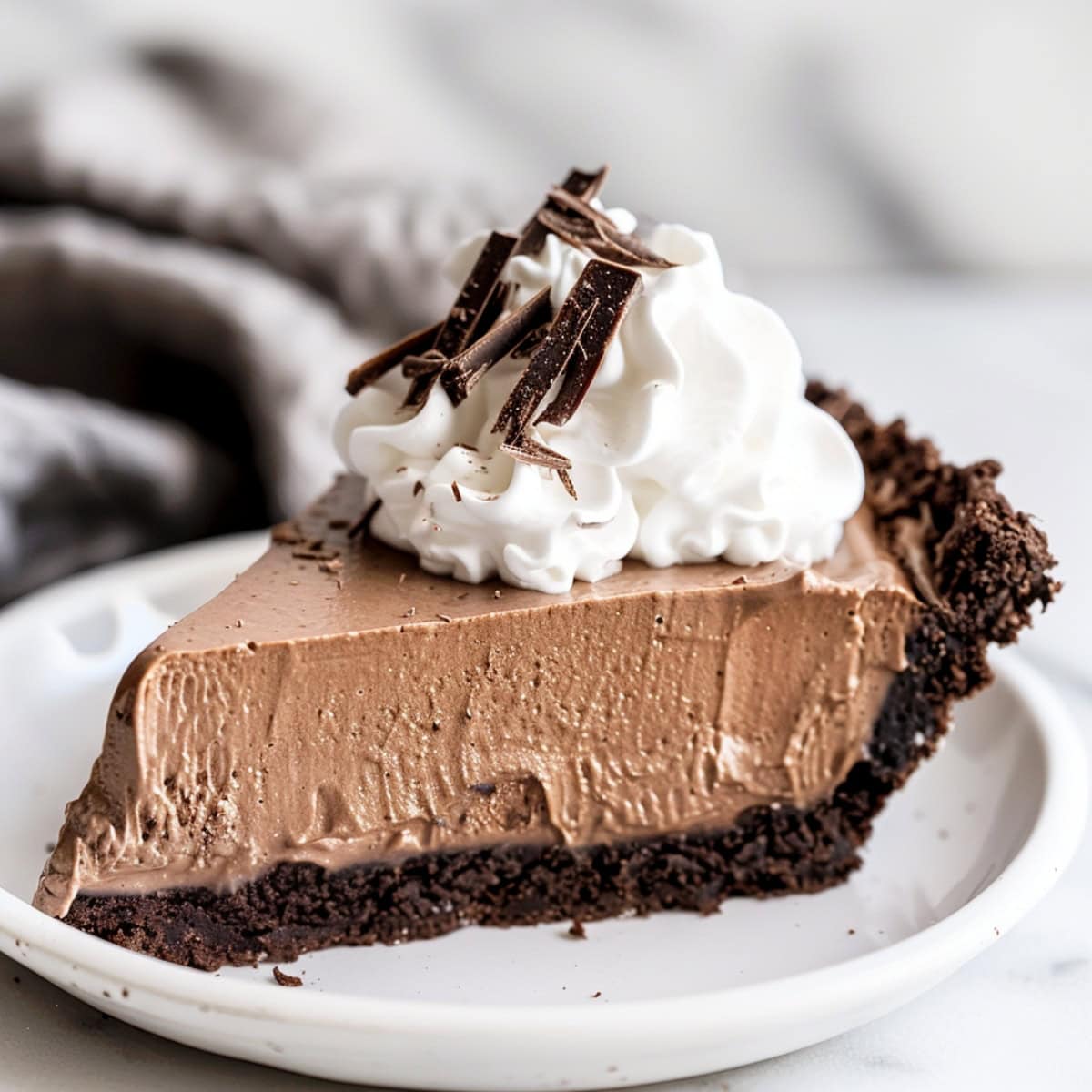 A slice of French silk pie on a white plate, showing the smooth layers of chocolate filling, topped with whipped cream
