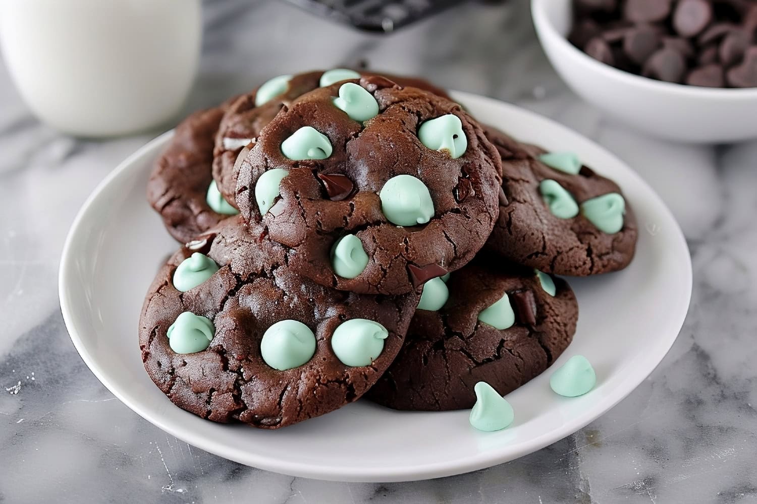 A plate of cookies with green and brown chips served with milk on a white marble countertop.