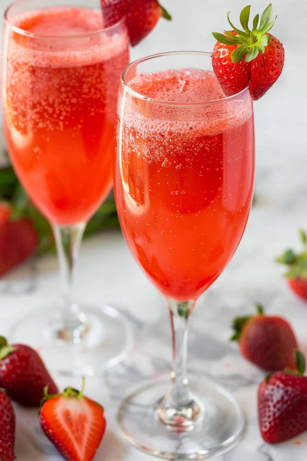Two glasses of bubbly sparkling wine garnished with fresh strawberries.