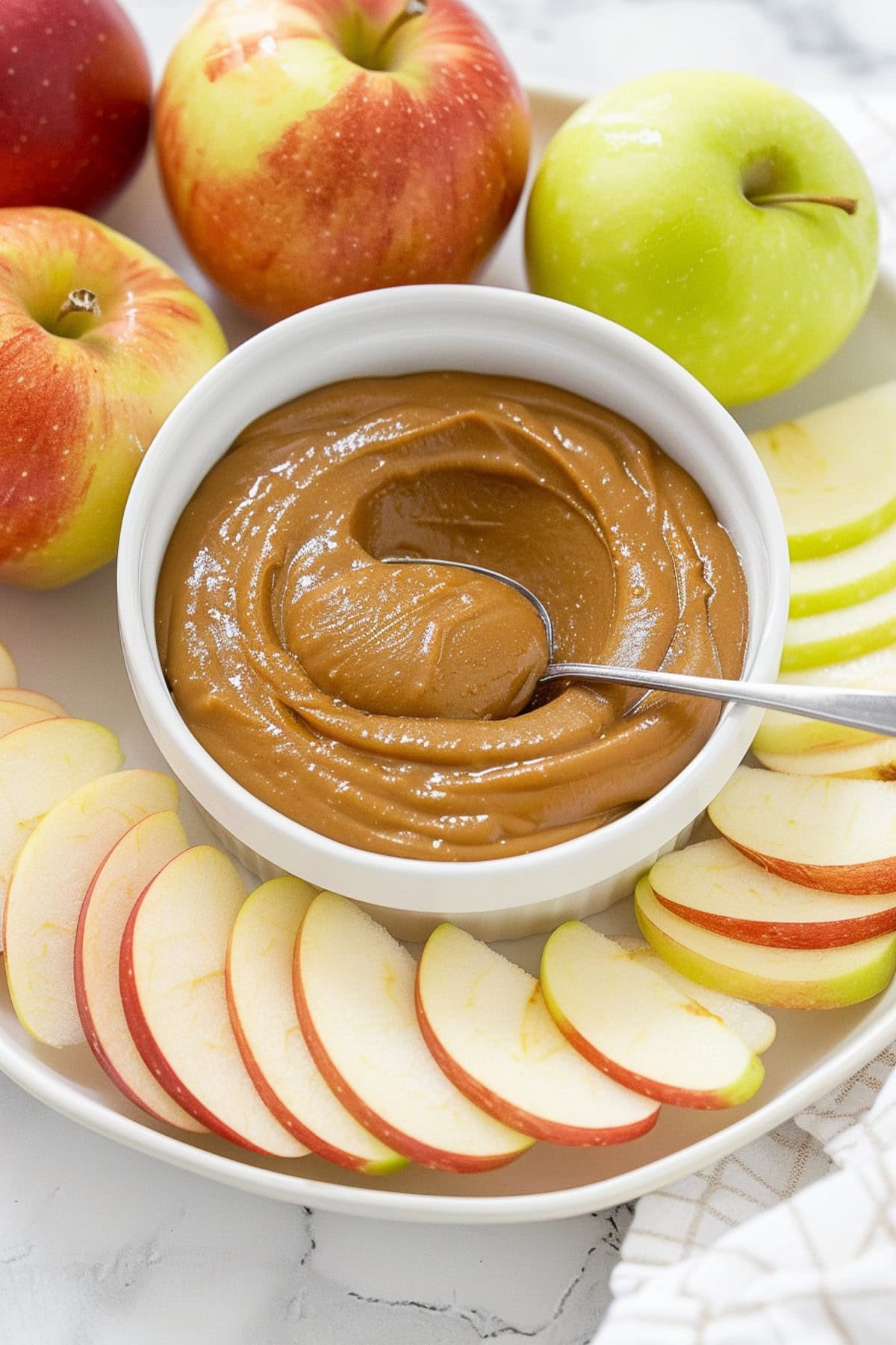 A white ceramic bowl filled with rich caramel dip, with a few apple slices