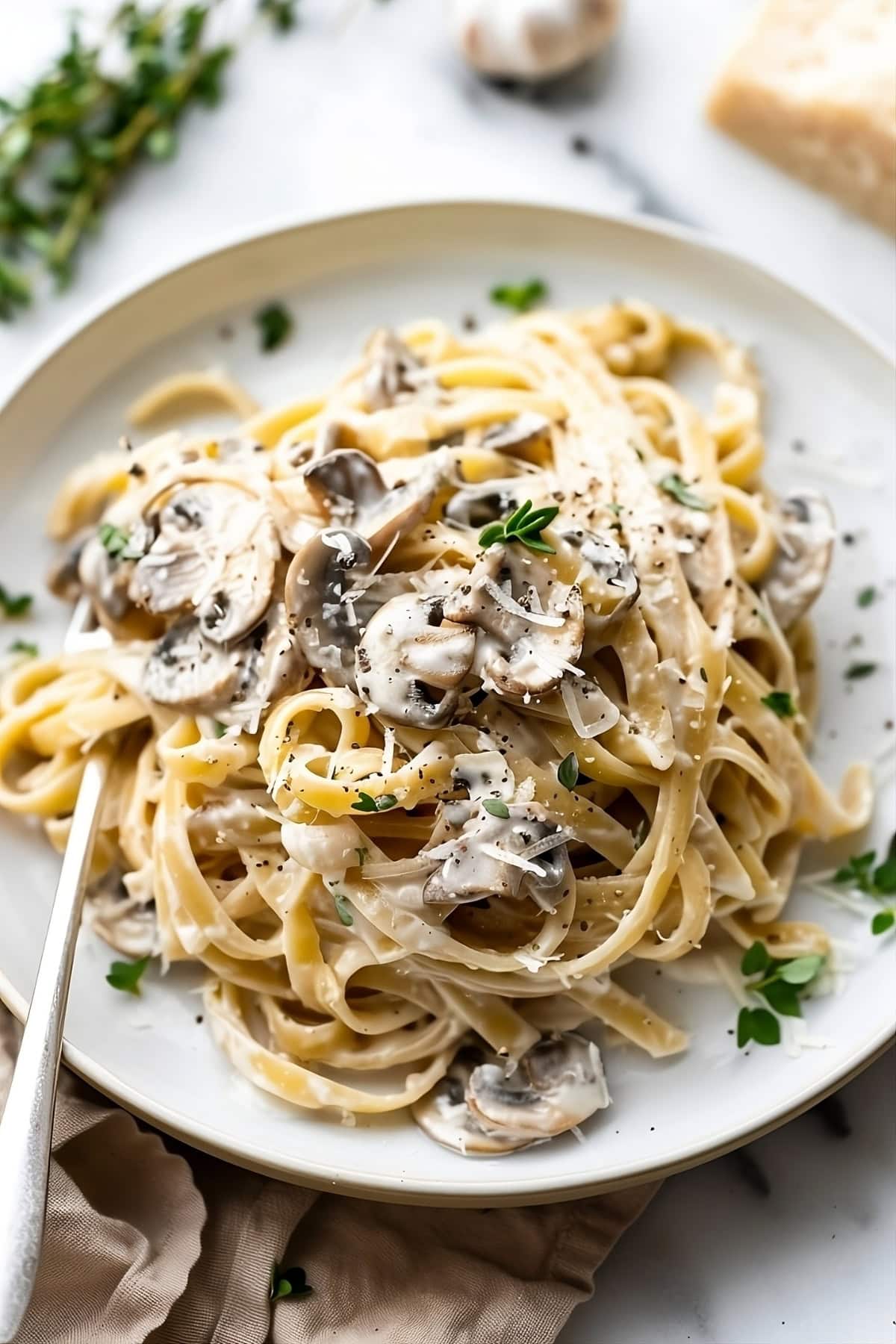 Creamy mushroom pasta in a white plate garnished with parmesan cheese.