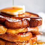 Super Close Up of Stack of Eggnog French Toast with Butter, Powdered Sugar, and Cinnamon with Maple Syrup Dripping Down the Stack